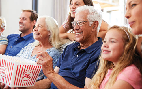 A group of people, including a man and a woman, are sitting on a couch and watching TV. The man is holding a bag of popcorn. AI generated content