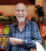 A man with a beard and a blue plaid shirt is smiling in front of a fruit stand. AI generated content